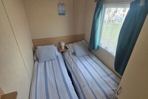 Habitació petita amb dos llits, una taula de nit amb una làmpada, una finestra amb cortines i un cartell penjat a la paret.
