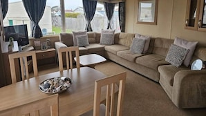 A furnished living area with a sofa, chairs, a dining table, a TV, and a ceiling fan.