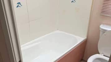 Une salle de bain avec une baignoire, des toilettes et des murs carrelés.