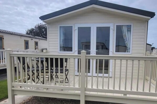 A mobile home with a deck, a covered patio, and a fenced area.