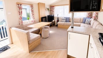 A modern living room with a sofa, a TV, a dining table, and a kitchen area with a microwave.