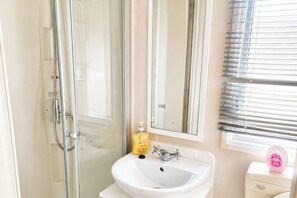 A bathroom with a glass shower enclosure, a white sink, a mirror, and a toilet with a pink decorative item on top.