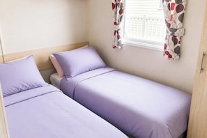 A single room with two beds, a window with curtains, and a wooden door.