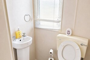 A small bathroom with a toilet, sink, and window. - 3 Bed Caravan - Sleeps 8 - Free Parking (Skegness)