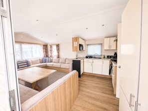A compact RV interior with a kitchenette, a dining area, and a seating area with curtains. - 3 Bed Caravan - Sleeps 8 - Free Parking (Skegness)