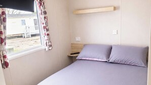 Ett sovrum med en säng, ett nattduksbord, ett fönster med gardiner och utsikt över ett hus utanför.