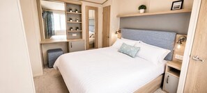 A bedroom with a bed, a wardrobe, a mirror, and a shelf with plants.