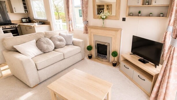 A living room with a sofa, a TV, a fireplace, and a kitchen area in the background.