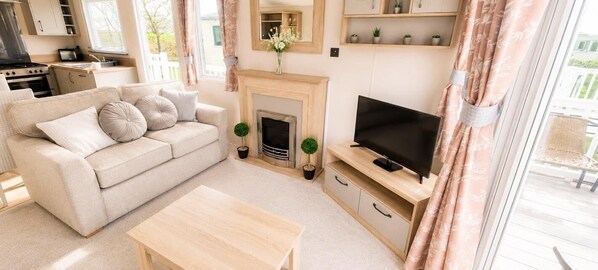 A living room with a sofa, a TV, a fireplace, and a kitchen area in the background.