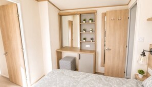 A bedroom with a bed, a desk with a mirror, a wardrobe, and a small stool.