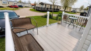 Une terrasse dotée de chaises en osier, d’une petite table et offrant une vue sur un quartier résidentiel avec ses maisons et ses voitures garées.