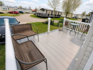 A deck with wicker chairs, a small table, and a view of a residential area with houses and parked cars.