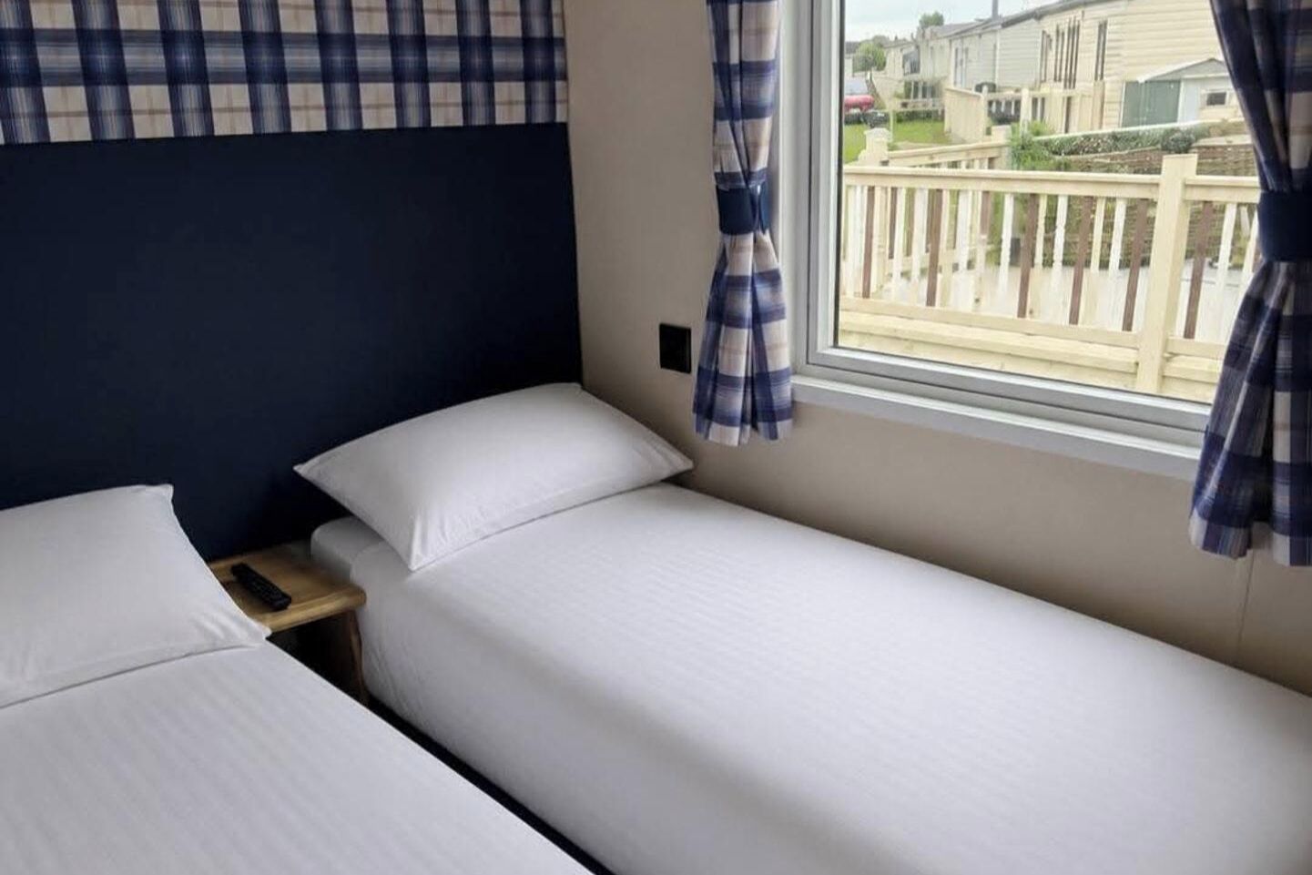 A twin room with two beds, a window with curtains, and a view of a residential area.