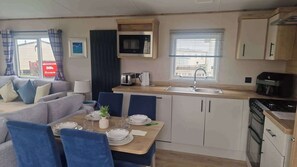 A compact kitchenette with a microwave, toaster, and sink, a dining area with a table set for two, and a living area with a sofa and chairs. - 3 Bed - Sleeps 8 - Family & Pet Friendly (Skegness)