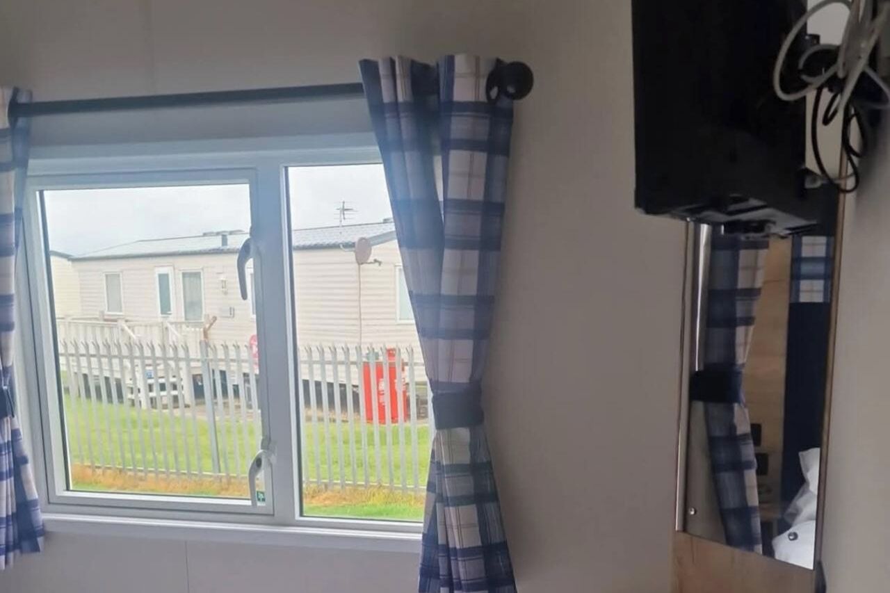 A room with a window, curtains, and a wall-mounted television.