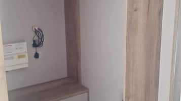 Une pièce comprenant une armoire en bois, un petit bureau avec des tiroirs, un portant à vêtements et une poubelle.