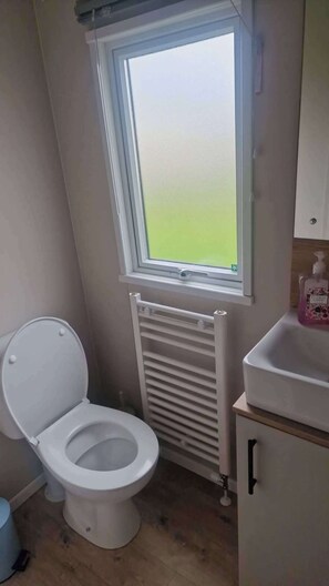 A small bathroom with a toilet, a window, a radiator, and a sink. - 3 Bed - Sleeps 8 - Family & Pet Friendly (Skegness)