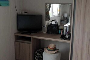A small room with a television on a wooden stand, a mirror above a sink, and a suitcase on the floor. - 3-bed Caravan - Sleeps 8 - Pet Friendly - Parking (Skegness)