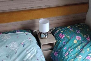 A room with two beds, each with floral bedding, a bedside table with a lamp, and a wooden headboard. - 3-bed Caravan - Sleeps 8 - Pet Friendly - Parking (Skegness)