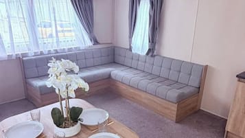 Un coin salon avec un banc rembourré, une table à manger dressée avec des assiettes et des couverts, et un pot d’orchidée.