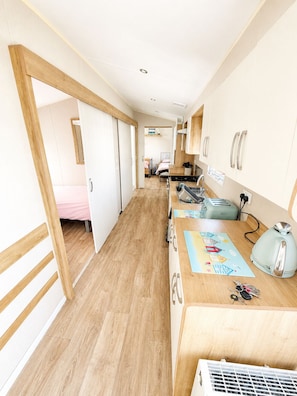 Ein schmaler Flur führt zu einem Schlafzimmer mit einem Bett, einer Küchenzeile mit einem Herd und einem Badezimmer mit einer Toilette.