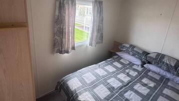 A small, single-bed room with a window, a wooden wardrobe, and a ceiling light fixture.