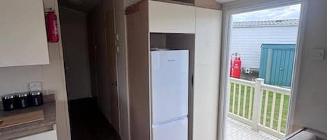 Una kitchenette compacta con refrigerador, una pequeña encimera y una puerta corredera que da a un balcón.