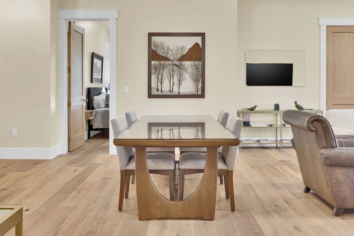 Un comedor con una mesa rectangular y seis sillas, un televisor montado en la pared y un sofá al fondo.