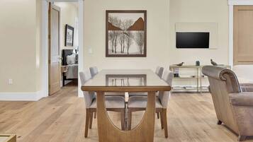 Un comedor con una mesa rectangular y seis sillas, un televisor montado en la pared y un sofá al fondo.
