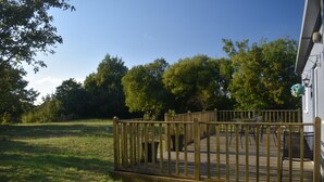 Eine Holzterrasse mit Geländer, umgeben von Gras und Bäumen.