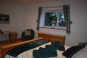 A bedroom with a bed, a chair, a dresser, and a window with curtains.