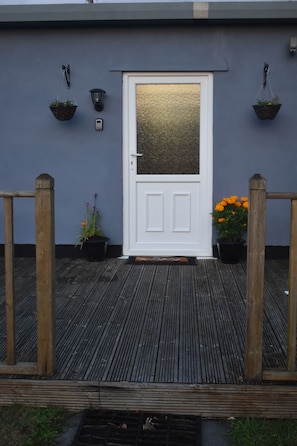 A white door with a textured glass panel, flanked by two hanging baskets and a wall-mounted light fixture.