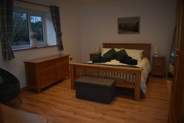 A bedroom with a wooden bed, a nightstand, a dresser, a window with curtains, and a painting on the wall.