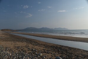 A beach with a rocky shoreline, calm water, and distant mountains. - Snowdonia Riverside Cabin with Private River (Caernarfon)