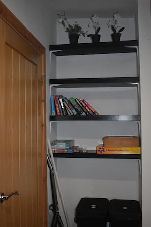 A room with a wooden door, a white wall, and a black shelf unit with books and a puzzle box.