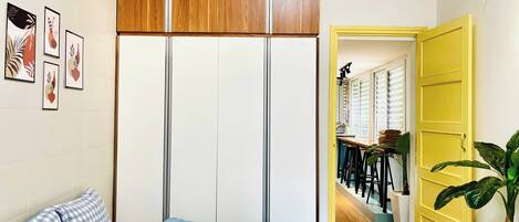 A bedroom with a bed, a wardrobe, and a yellow door leading to a dining area.