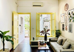 A room with a sofa, a coffee table, a window with a view, and a wall with framed artwork. - The Hanoian Local Nest - Old Quarter Heart - 5' to Hoankiem Lake & Beer street (Hà Nội)