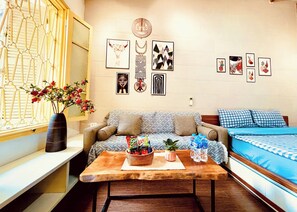 A room with a sofa, a coffee table with snacks, a bed with checkered bedding, and wall art. - The Hanoian Local Nest - Old Quarter Heart - 5' to Hoankiem Lake & Beer street (Hà Nội)