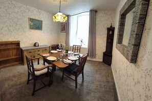 A dining room with a wooden table set for four, surrounded by chairs, a wooden cabinet, and a wall clock.