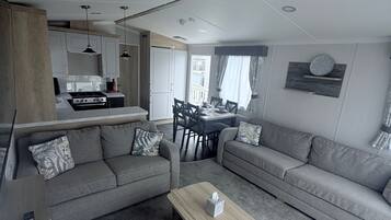 A modern living room with grey sofas, a wooden coffee table, and a dining area with a table and chairs.