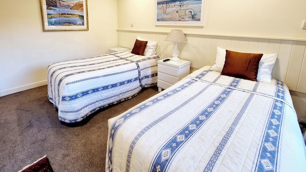 Habitación de hotel con dos camas, una mesita de noche con lámpara y dos cuadros en la pared.