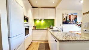 Una cocina moderna con armarios blancos, horno empotrado, salpicadero verde y encimera de granito.
