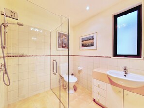 Un baño moderno con ducha de vidrio, inodoro, lavamanos y dos cuadros en la pared.