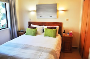 A hotel room with a bed, bedside tables, a nightstand, a painting on the wall, and a window with curtains. - Penrich Court (Queenstown)