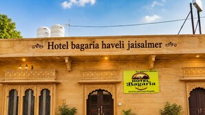 Fachada de hotel con un cartel que indica 'Hotel Bagaria Haveli Jaisalmer' y 'Habitaciones con aire acondicionado y sin aire acondicionado disponibles'.