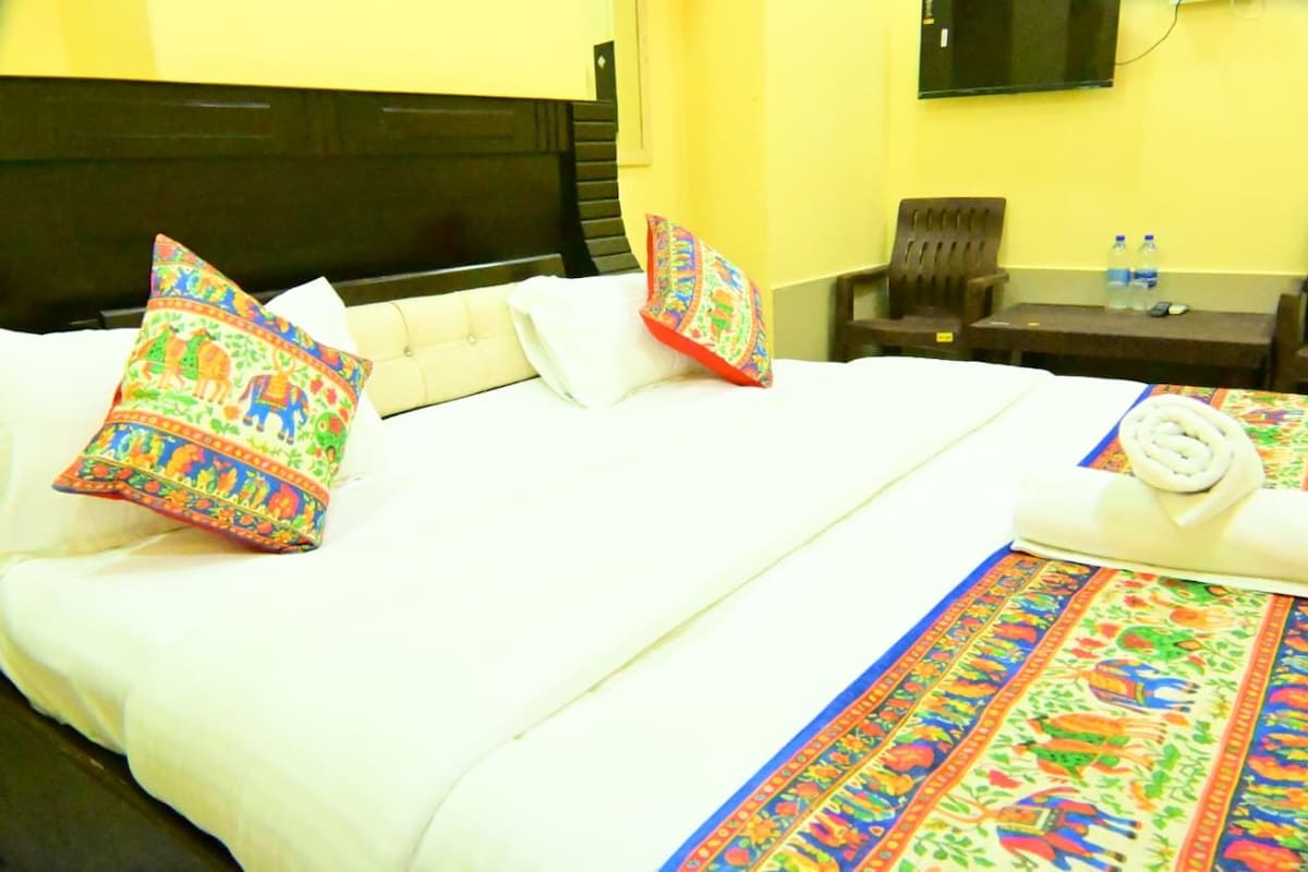 Une chambre d’hôtel avec un lit, des oreillers, une petite table avec des bouteilles d’eau et une chaise.