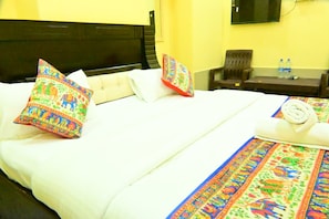 A hotel room with a bed, pillows, a small table with water bottles, and a chair. - Hotel Bagaria Haveli (Jaisalmer)