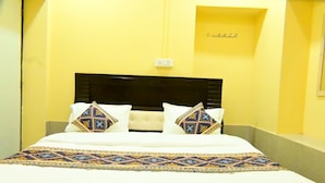 Una cama con cabecera, dos almohadas y una colcha estampada en una habitación con paredes amarillas.