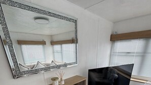 Ein kompakter Wohnbereich mit Fernseher, kleinem Kühlschrank, Spiegel und einem Fenster mit Jalousien.