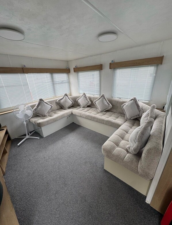 A compact living space with a sofa set, a standing fan, and a window with blinds.